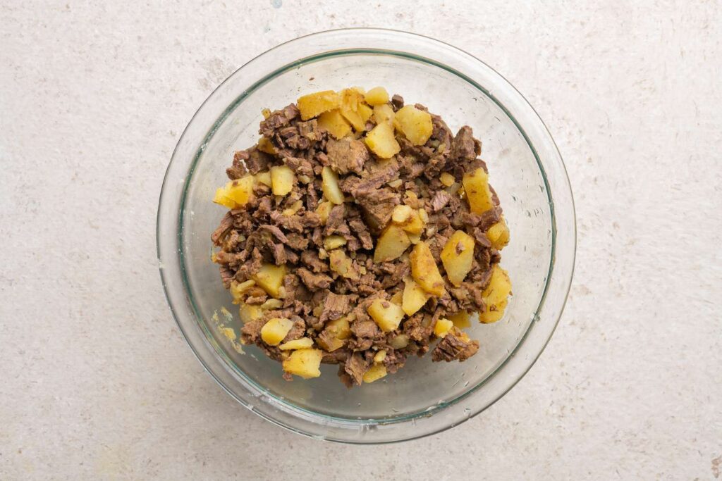 A mixture of plant-based ground beef and mashed potatoes being prepared for empanada filling.